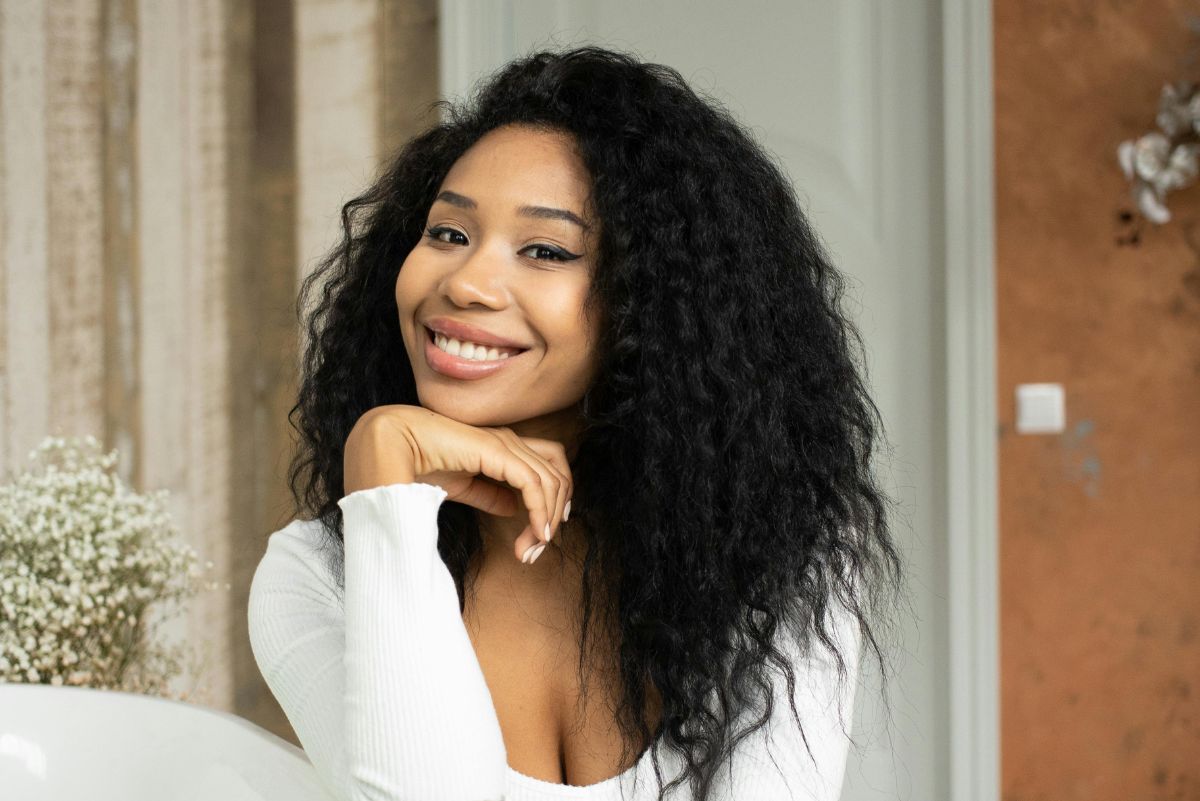 woman in a white top leaning on the side of a bathtub smiling