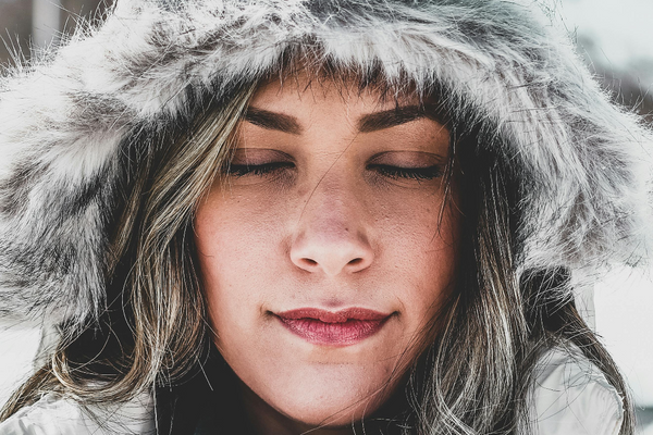 a model wearing a furry hood with her eyes closed on a snowy background