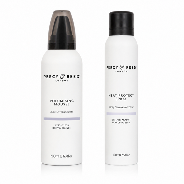 Two white cylindrical bottles of Percy Reed London hair styling products on a white background: Volumising Mousse with a translucent smoky cap and Heat Protect Spray with a black cap.