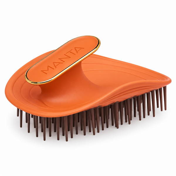 An orange Manta Detangling Hairbrush with dark brown bristles and a gold trim on the handle, shown on a clean white background.