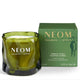 An olive green glass scented candle with a wick and white wax, shown next to its matching green packaging box. The brand NEOM is clearly visible on both the candle and the box.