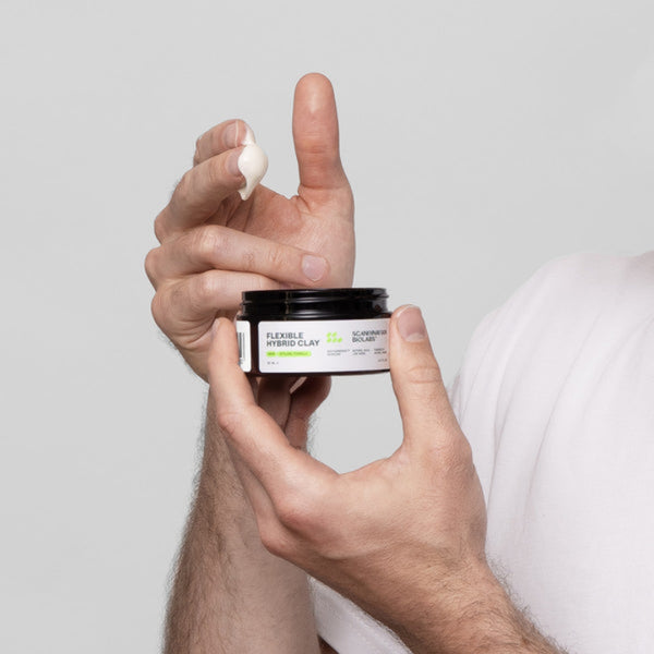 Hand holding a jar of hair product with a white background