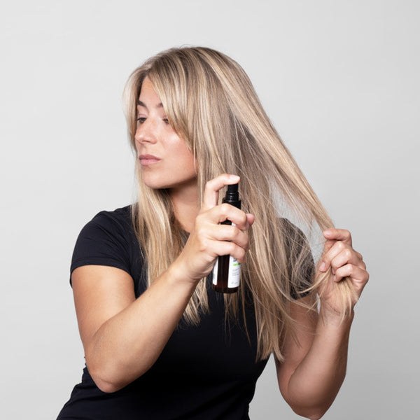 Woman applying hair product to her blonde hair against a plain background