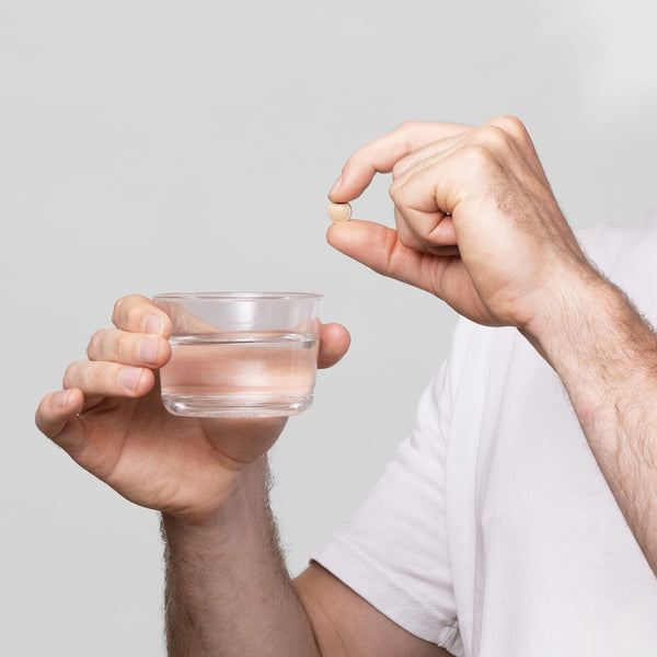 Hand holding a small glass of water against a plain background