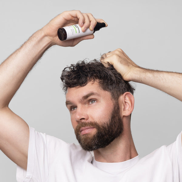 Man applying hair product with a bottle against a gray background