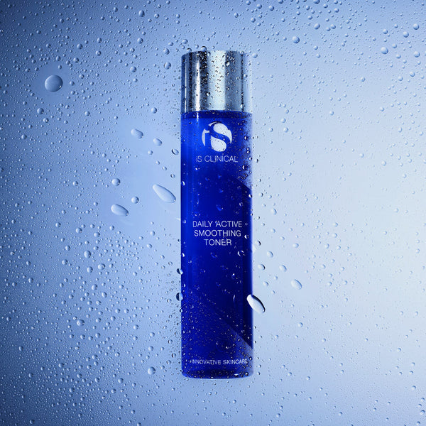 A bottle of e:CLINICAL Daily Active Smoothing Toner with a metallic silver cap and a deep blue body, shown against a cool blue gradient background with water droplets on a glass-like surface.