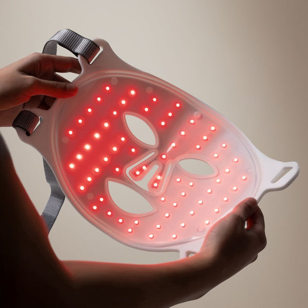 LED face mask with red lights held by a person against a neutral background
