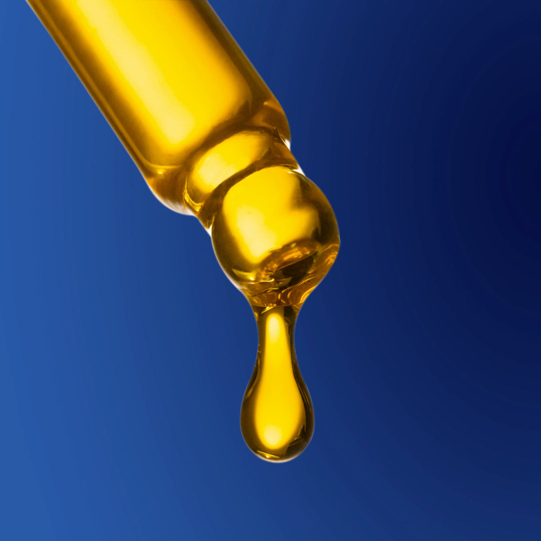 Glass dropper with yellow liquid dripping against a blue background