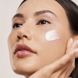 a woman applying cream to her cheek 