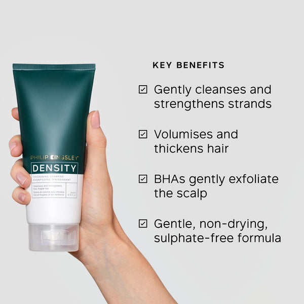 Hand holding a tube of Philip Kingsley Density product with key benefits listed on a gray background