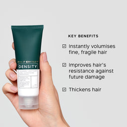 Hand holding a tube of Philip Kingsley Density conditioner with key benefits listed on a gray background