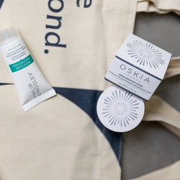 Cosmetic products including a tube and a round container on a branded tote bag.