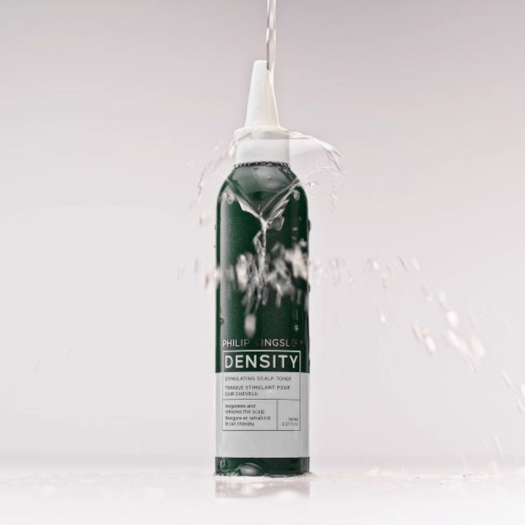A single cylindrical bottle of DENSITY brand product stands upright on a white surface against a light gray studio background, with water splashing around it and a clear stream entering the top opening.