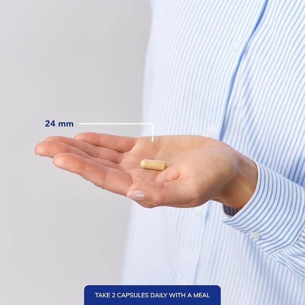 A person in a light blue striped shirt holds an open hand showing a small beige capsule, with a measurement label reading 24 mm and a blue text note at the bottom that says TAKE 2 CAPSULES DAILY WITH A MEAL.