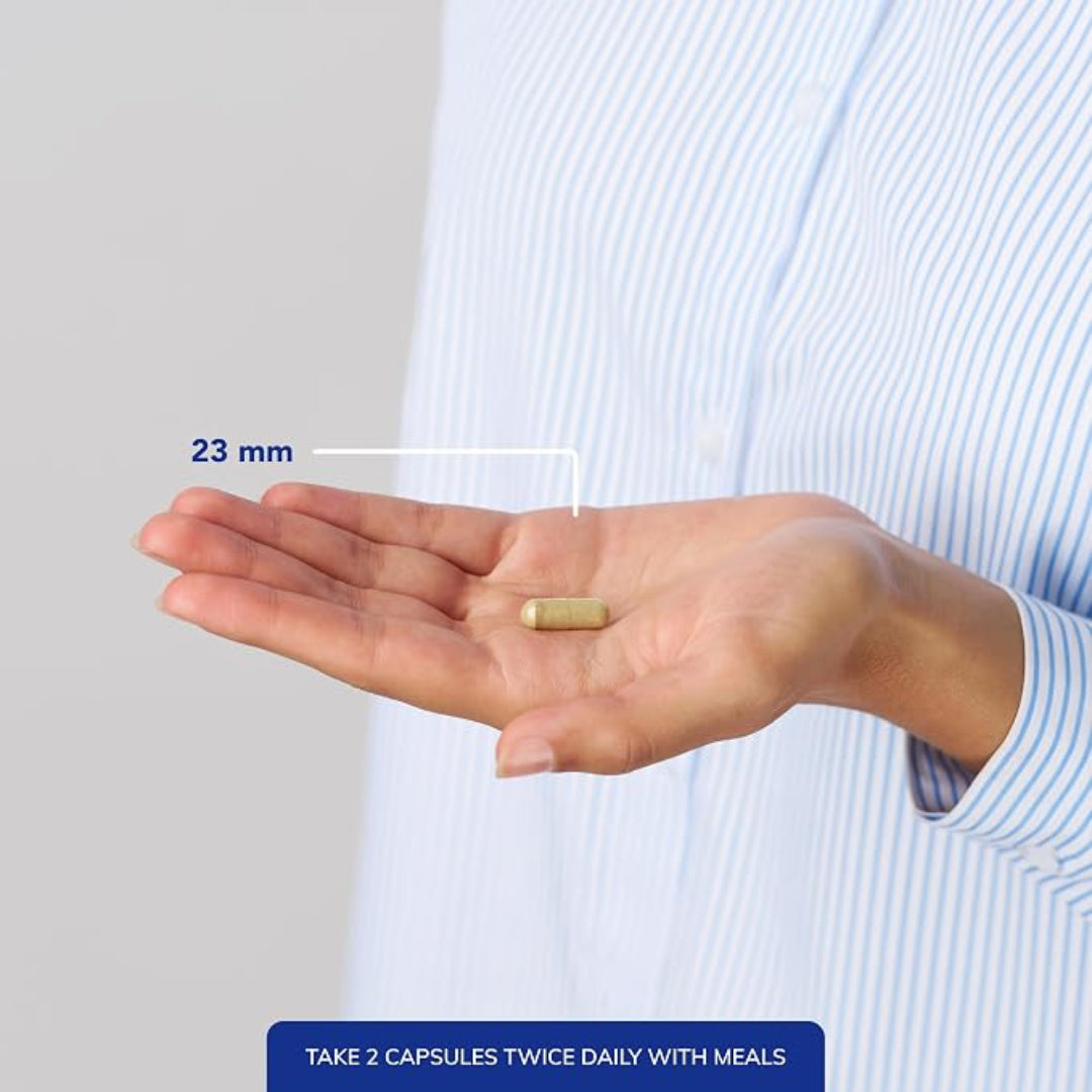 A person in a light blue and white striped shirt holds an open hand showing a single capsule pill, with a white line and blue text indicating its size is 23 mm. A dark blue banner at the bottom reads 'TAKE 2 CAPSULES TWICE DAILY WITH MEALS'.