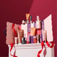 A Catineal skincare advent calendar set displayed on a white pedestal against a deep burgundy background. The set includes a large pink and white advent calendar box with numbered doors, several individual skincare products in pink, orange, purple, and black packaging, and red ribbon accents.