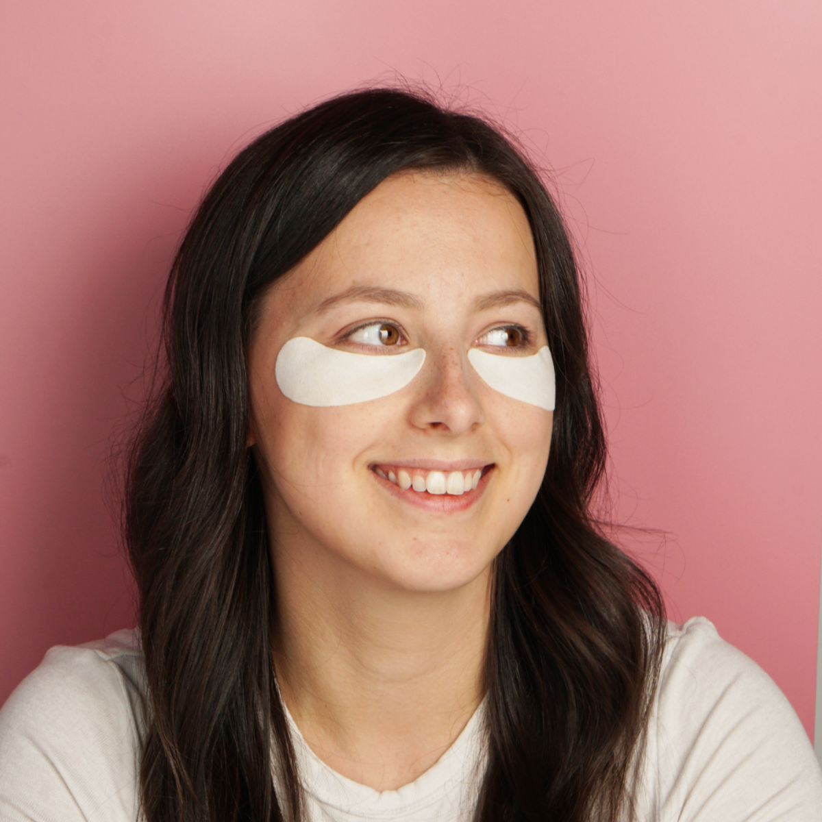 Woman wearing eye patches against a pink background