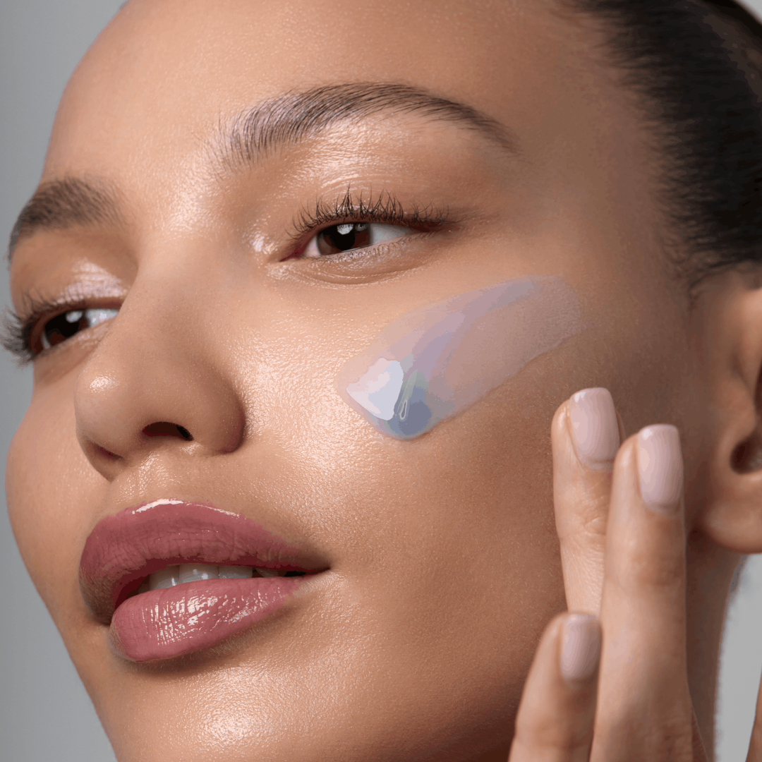 Close-up of a woman applying a skincare product to her face with a neutral background