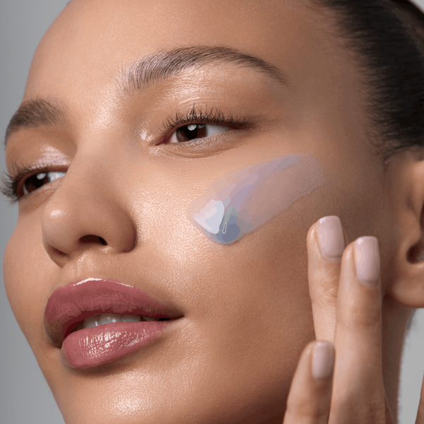 Close-up of a woman applying a skincare product to her face with a neutral background