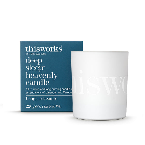 A white glass candle jar with a subtle embossed logo next to its dark teal-blue packaging box. The box features white text reading 'thisworks deep sleep heavenly candle'.