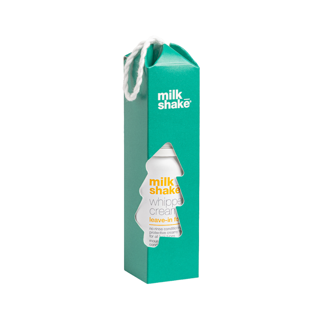 A tall teal-green Milk Shake leave-in whipped cream carton package with a white hanging loop and a die-cut window showing the product bottle inside, on a plain white background.