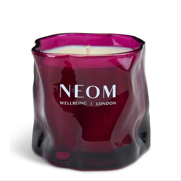 A NEOM Wellbeing London scented candle in a wavy, wavy textured dark magenta glass jar with white wax and a single wick, on a clean white background.