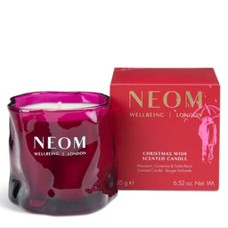 A NEOM Wellbeing London 'Christmas Wish' scented candle in a deep magenta glass jar, shown next to its red packaging box with gold lettering on a white background.