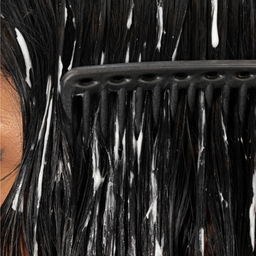 Close-up of a comb through wet hair with white conditioner or shampoo being applied.