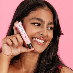 Woman holding a pink lip balm against a pink background