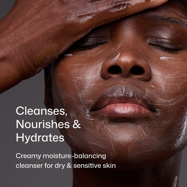 Close-up of a person with a dark complexion applying or wearing a creamy skincare cleanser, with text reading 'Cleanses, Nourishes & Hydrates' and 'Creamy moisture-balancing cleanser for dry & sensitive skin' on a dark gray background.