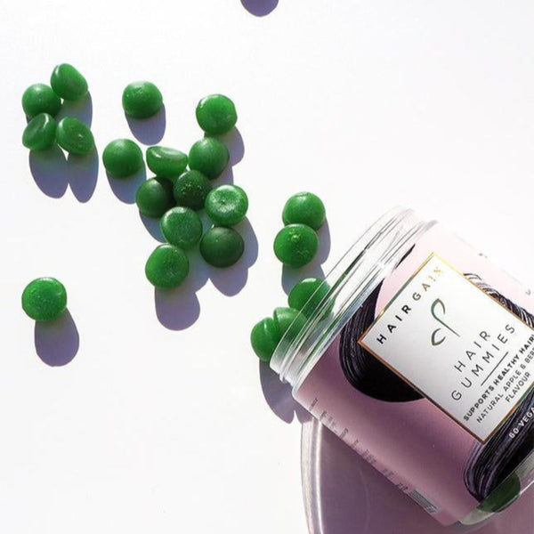 Pink container of hair gummies with green gummy bears on a white background