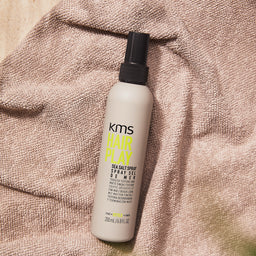 KMS Hair Play sea salt spray bottle on a textured surface
