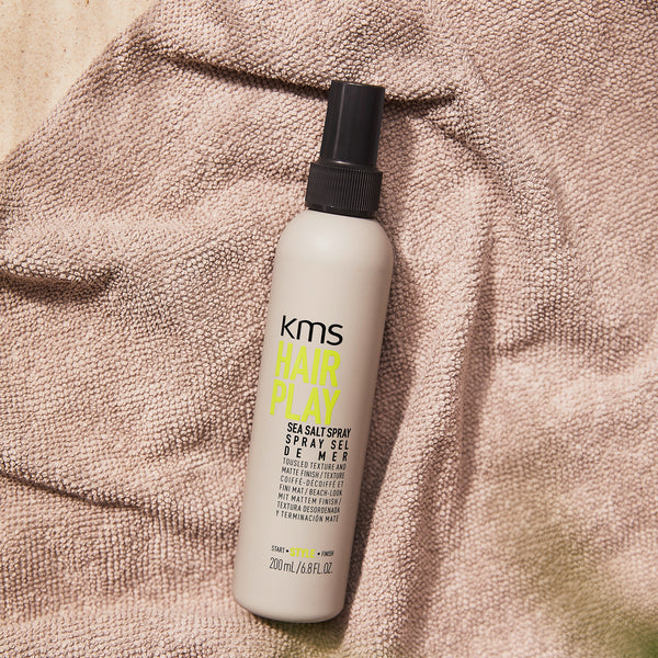 KMS Hair Play sea salt spray bottle on a textured surface