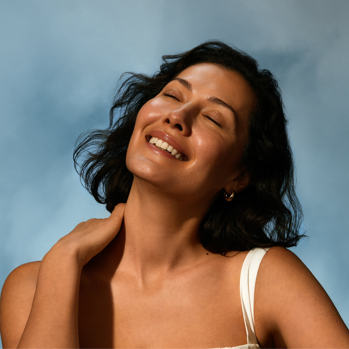 Woman with dark hair smiling against a blue sky