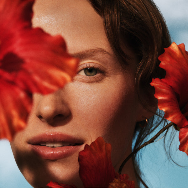 Close-up of a person with red flowers in front of their face, wearing a blue top.