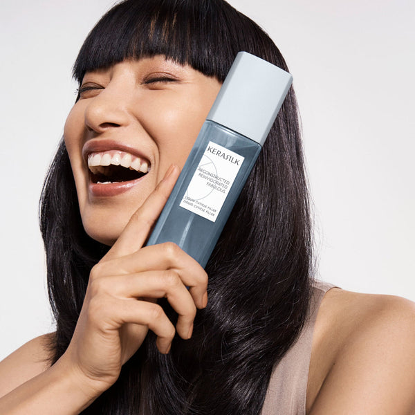 Woman holding a bottle of KeraSilk hair product against a white background