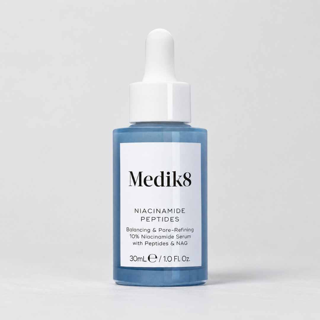 Medik8 Niacinamide Peptides Balancing & Pore-Refining Serum in a 30mL blue glass dropper bottle with a white label and white dropper cap, set against a light gray studio background.