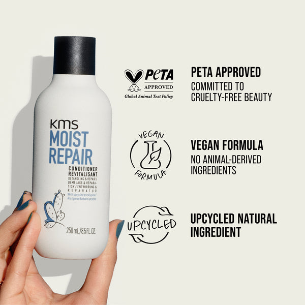 KMS Moist Repair conditioner bottle held by a hand with PETA approval and vegan formula labels on a light gray background.