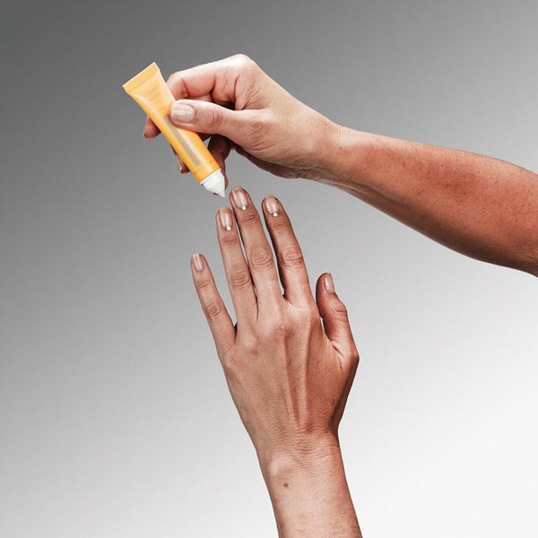 Hand applying a yellow tube of cream to another hand against a gray background
