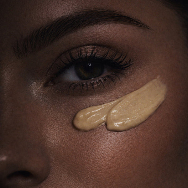 Close-up of a woman's face with two beige makeup swatches on her cheek.