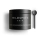 A matte black cosmetic jar labeled 'WILDSMITH SKIN' with white text reading 'ACTIVE REPAIR COPPER PEPTIDE CREAM,' shown on a white background with a matching black spoon to the right.
