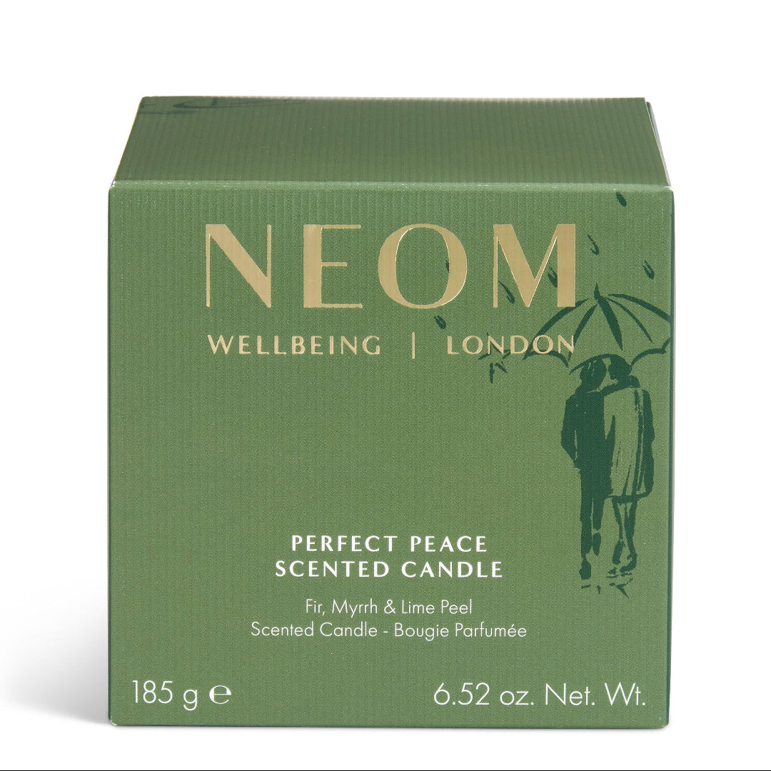 A square green box of NEOM Wellbeing London 'Perfect Peace' scented candle, featuring gold lettering and a dark green silhouette of a couple under an umbrella, on a white background.
