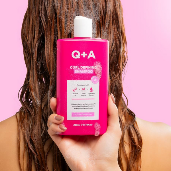Person holding a pink bottle of Q+A Curl Defining Shampoo against a pink background