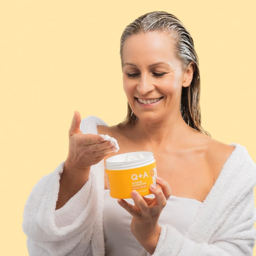 Woman in a white robe applying cream from a yellow container with 'Q+A' branding on a yellow background