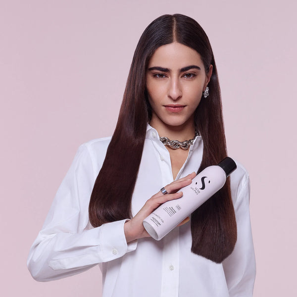 Woman holding a bottle of shampoo with a pink background