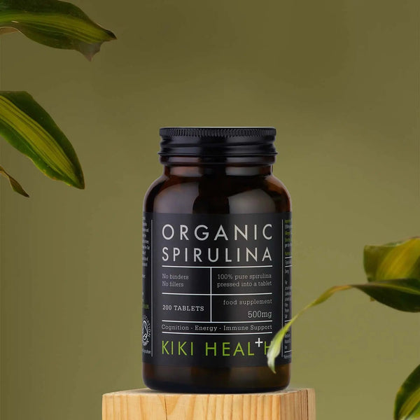 Bottle of Organic Spirulina by KIKI HEAL on a wooden block with green leaves in the background