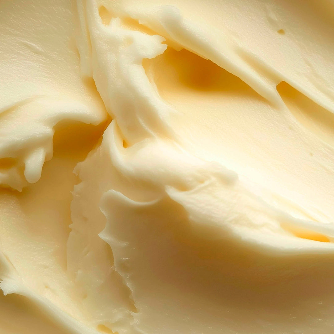 A close-up texture shot of creamy, pale yellow whipped cream or butter with soft folds and smooth lighting.