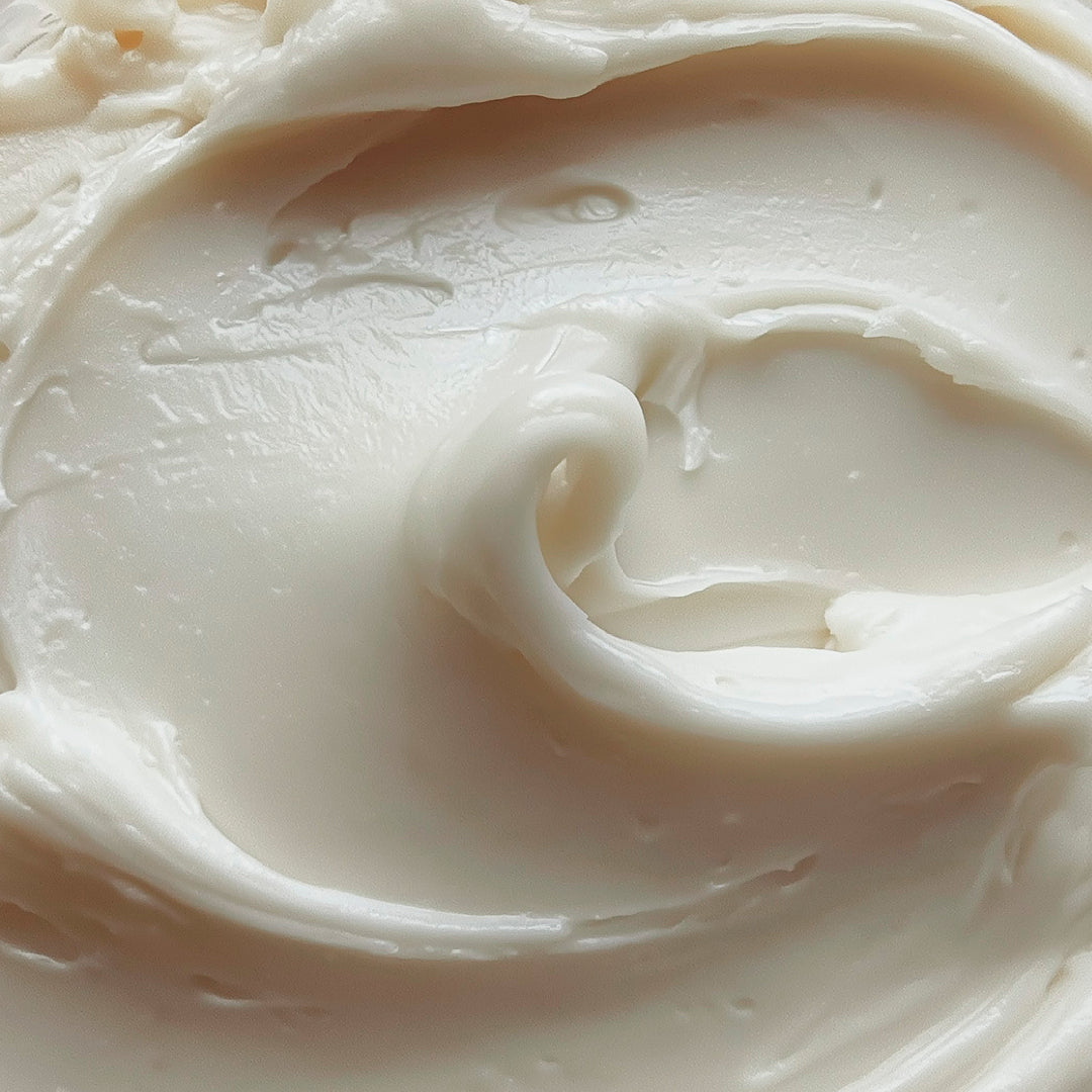 A close-up texture shot of a thick, creamy off-white cosmetic cream with smooth swirls and soft shadows.