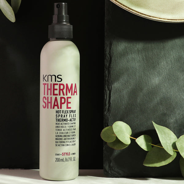 KMS Thermo Shape hair spray bottle with green leaves on a dark background