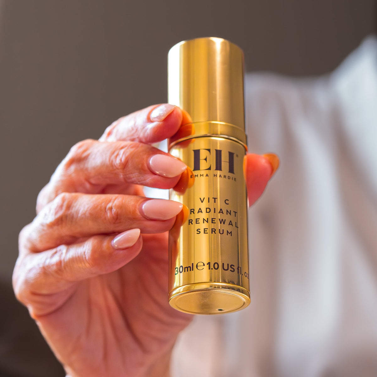 Gold Vit C Radiant Renewal Serum bottle held by a hand with neutral nail polish.